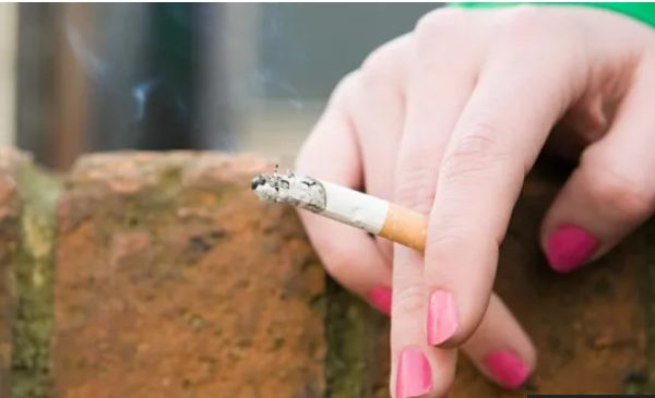 A hand with painted nails holding a lit cigarette