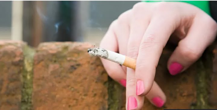 A hand with painted nails holding a lit cigarette